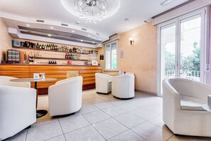 A modern bar area with a wooden counter, white leather seating, and a large window offering a view of greenery. - Villa Maria (Cesenatico)