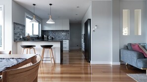 Una cocina moderna con una isla central, iluminación colgante y un comedor con sillas de madera.