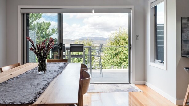 Comedor con una larga mesa de madera, sillas y vistas a una terraza exterior a través de un ventanal.