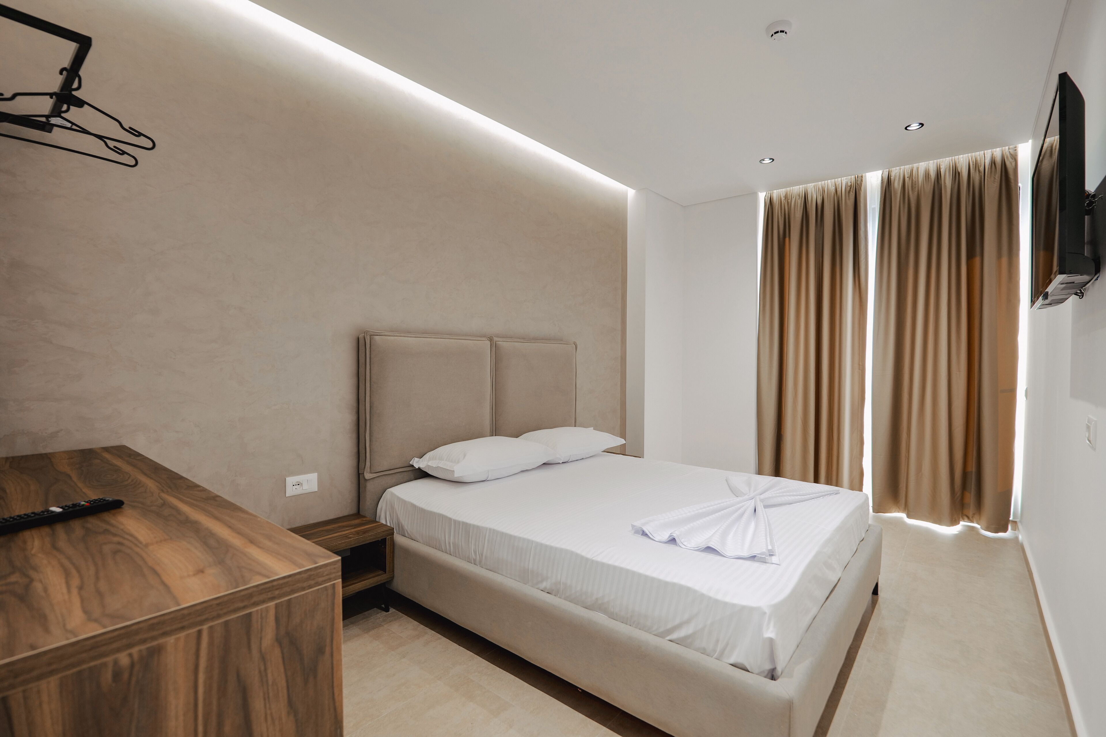 Una habitación de hotel moderna con un escritorio de madera, una cama con ropa blanca y un televisor montado en la pared.