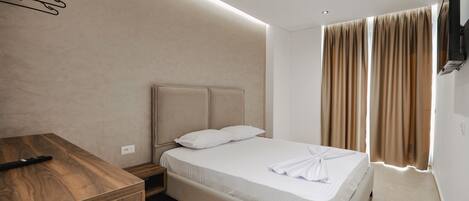 Una habitación de hotel moderna con un escritorio de madera, una cama con ropa blanca y un televisor montado en la pared.