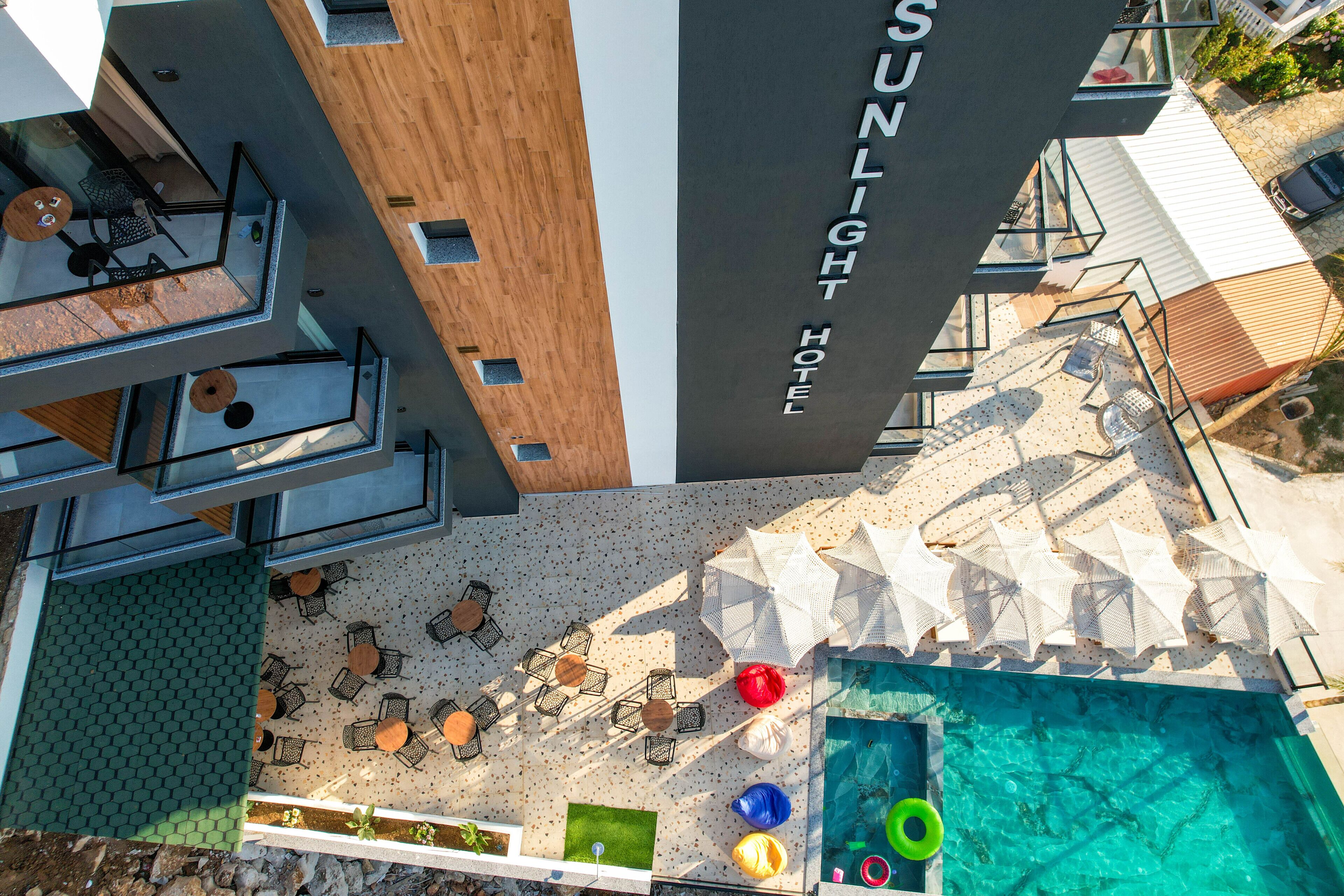 A rooftop pool area with lounge chairs and umbrellas, a wooden deck, and a sign for the Sunlight Hotel.