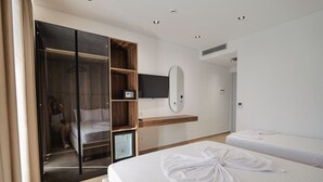 Une chambre d’hôtel moderne dotée d’un dressing, d’un téléviseur à écran plat, d’un miroir et de deux lits avec du linge de lit blanc.
