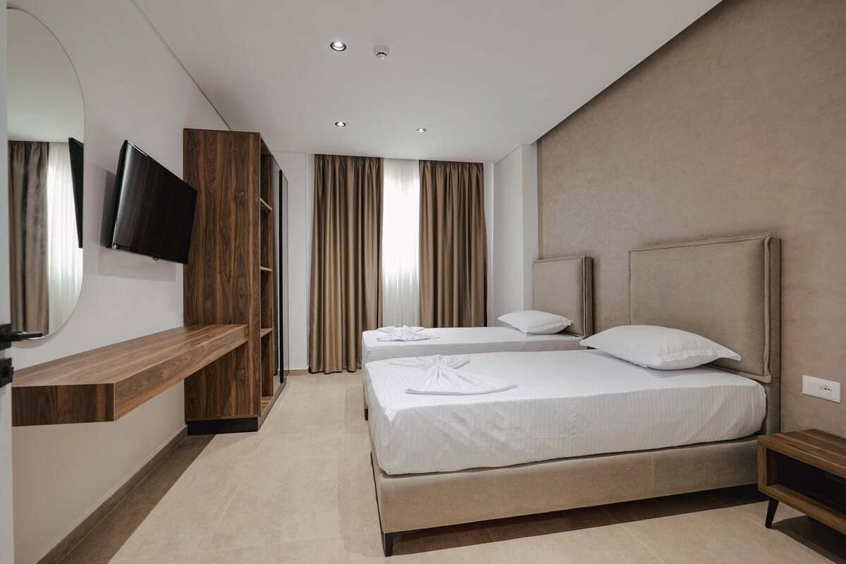 A modern hotel room with a large bed, a TV mounted on a wooden panel, and a built-in bench.