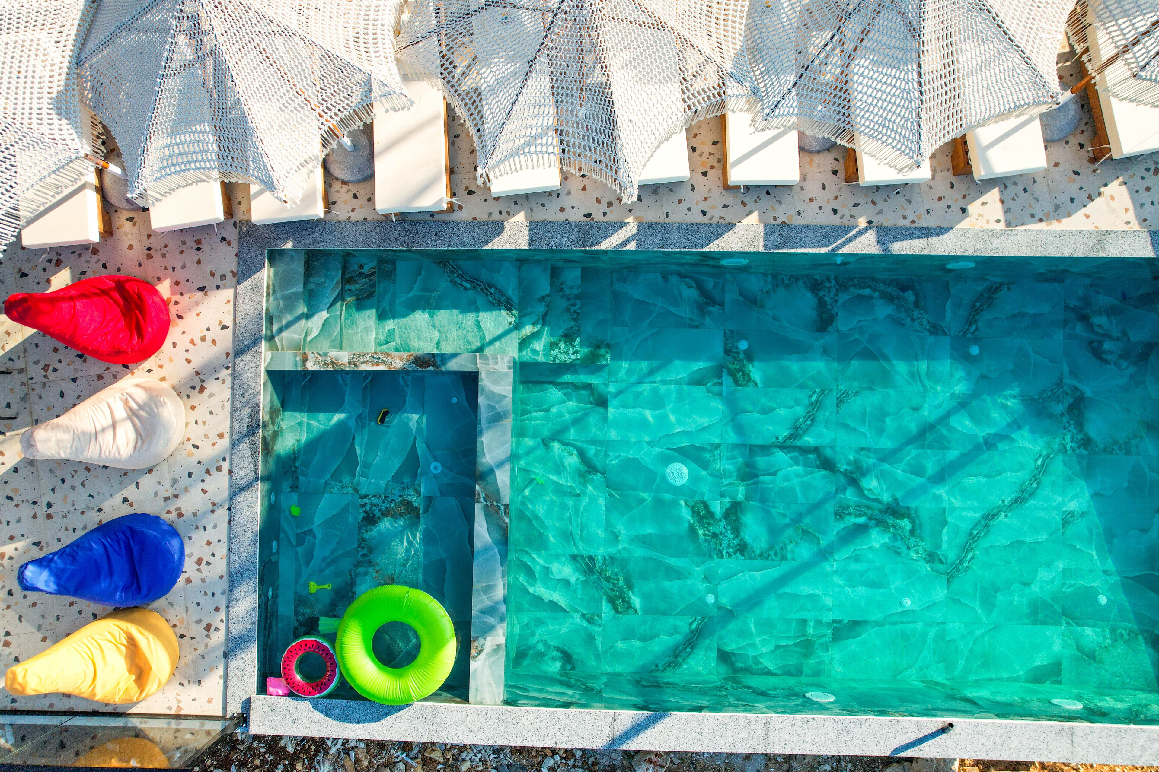 Une piscine à l’eau claire, entourée de chaises longues blanches et de parasols.