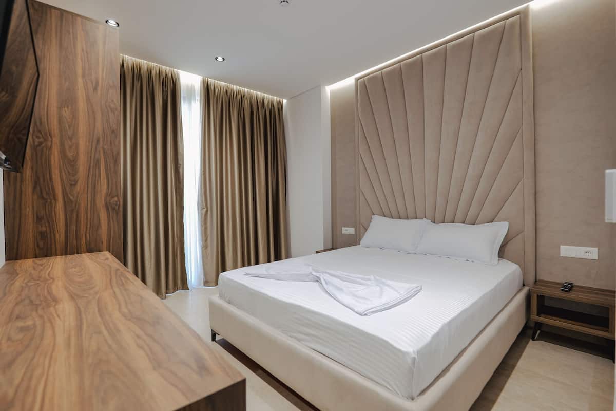 A modern hotel room with a large bed, wooden headboard, and a wooden desk.
