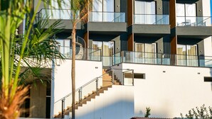 Un immeuble moderne à plusieurs étages, doté de balcons, d’un escalier et d’une structure rouge à sa base.