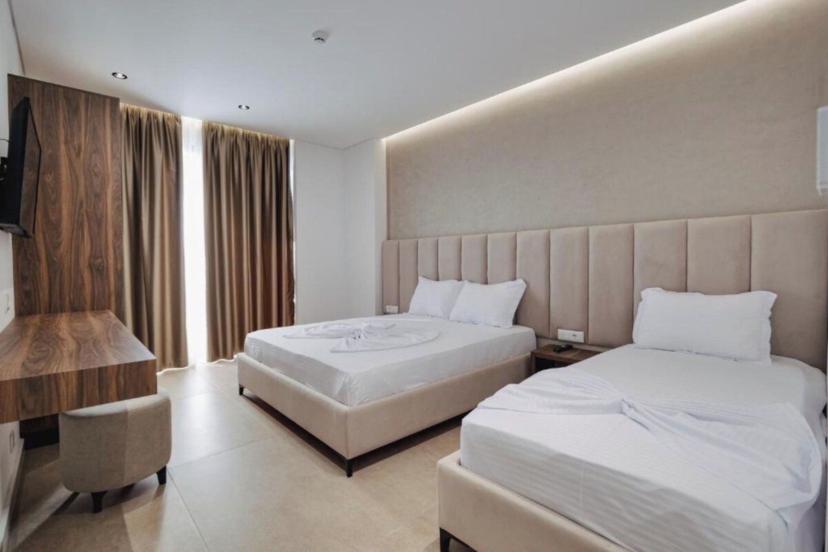 Habitación de hotel con dos camas, un escritorio de madera y un ventanal con cortinas.