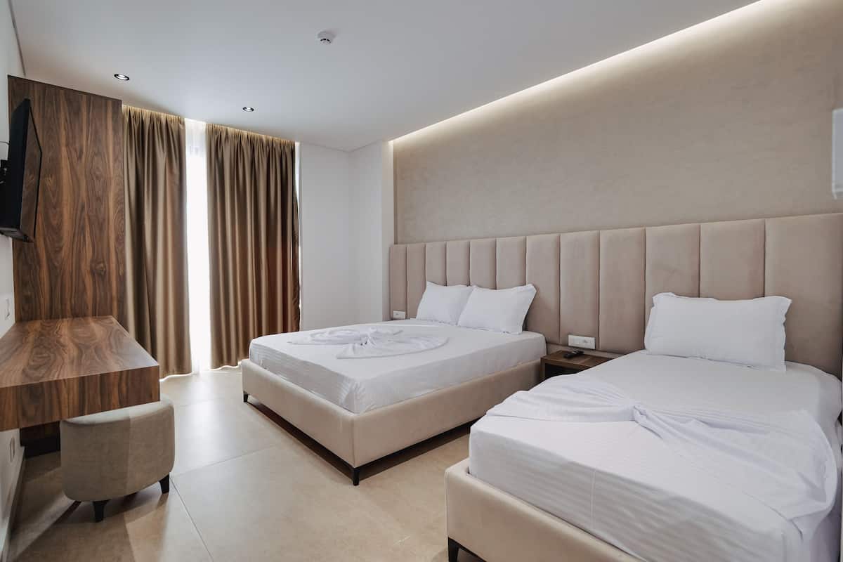 A hotel room with two beds, a wooden desk, and a TV.