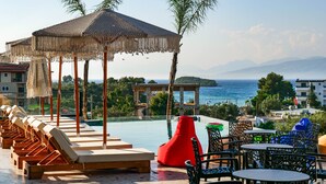 Un espace aménagé au bord de la piscine, avec des chaises longues, un fauteuil en forme de sac de haricots rouge et une vue sur la mer.