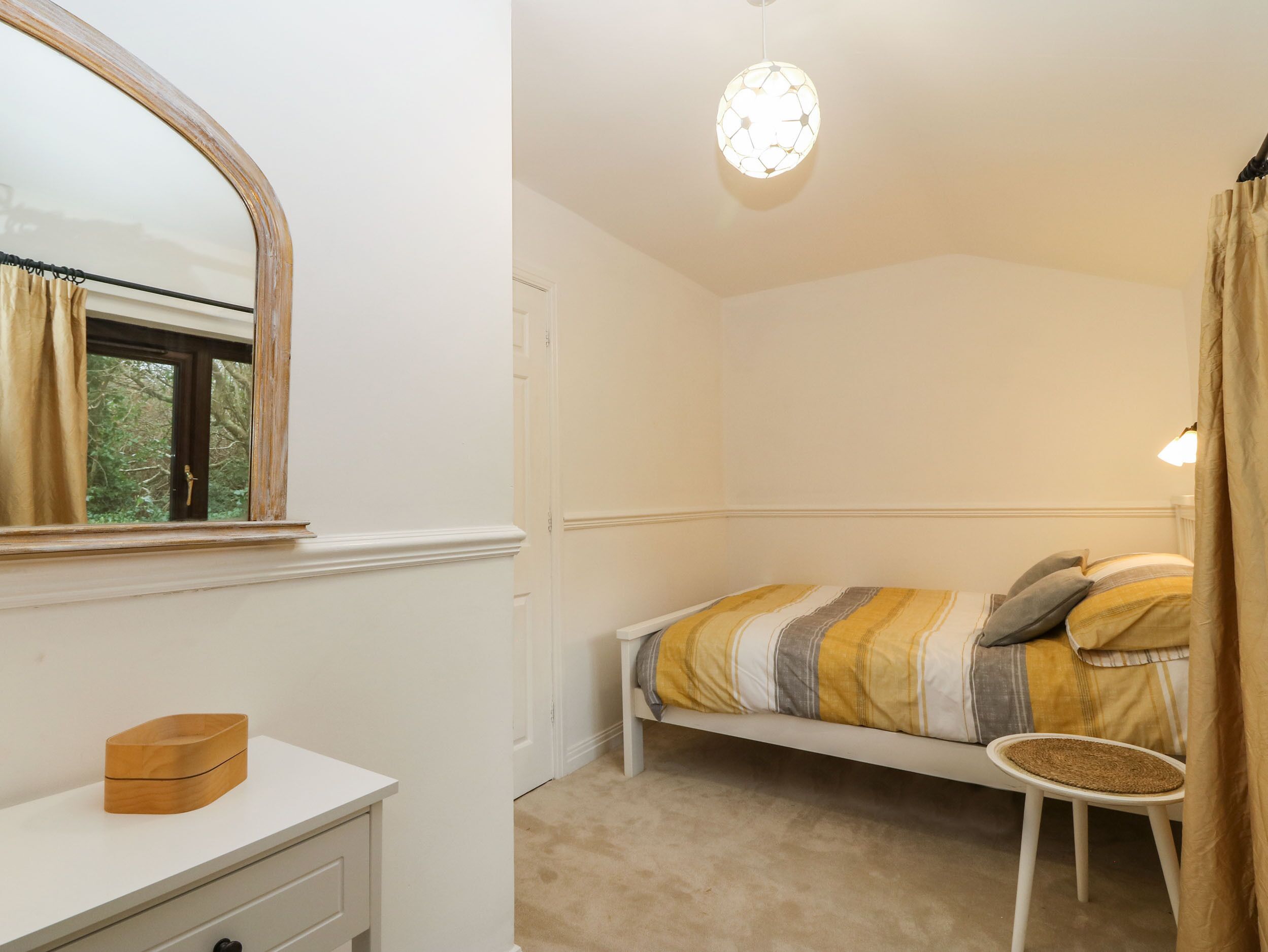 A bedroom with a bed, a bedside table, a mirror, a window, and a ceiling light.