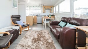 A compact living space with a kitchenette, a brown leather sofa, a wooden chair, and a dining table. - Wagtails (Dartmouth)
