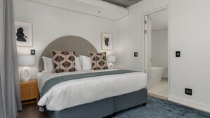 A modern bedroom with a large bed, a grey upholstered headboard, and a blue carpet. - Trendy Signature Apartment l Wifi l Balcony (Cape Town)