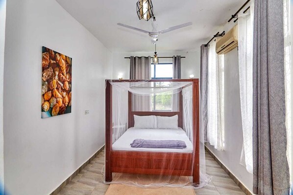 Un dormitorio con cama con dosel, ventilador de techo y un amplio ventanal con cortinas.