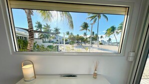 Ein Zimmer mit großem Fenster und Blick auf einen Strand, ein kleiner Tisch mit Lampe, ein Handtuch und eine Karte auf dem Boden.
