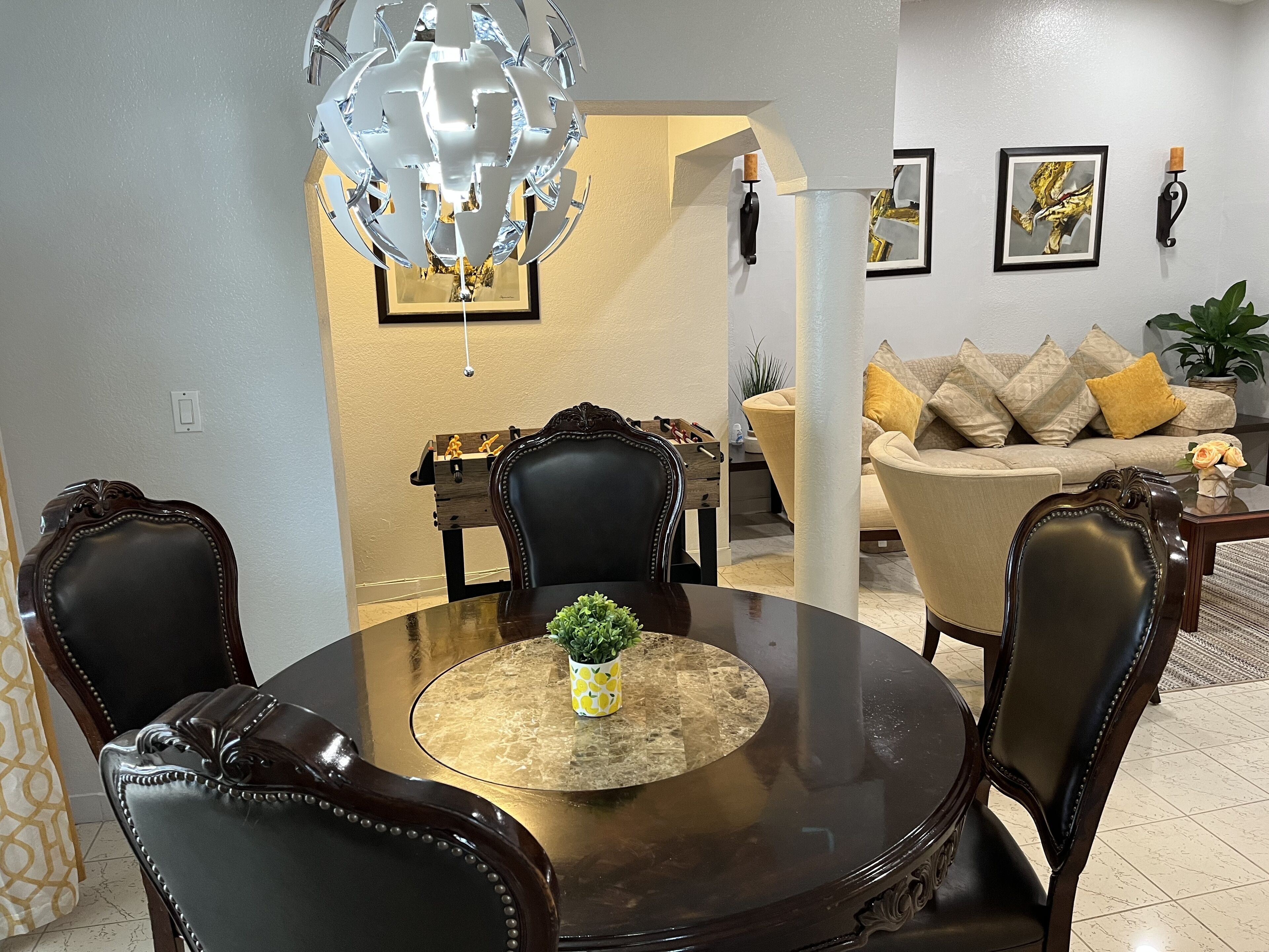 A dining area with a round table, chairs, a chandelier, and a sofa in the background.
