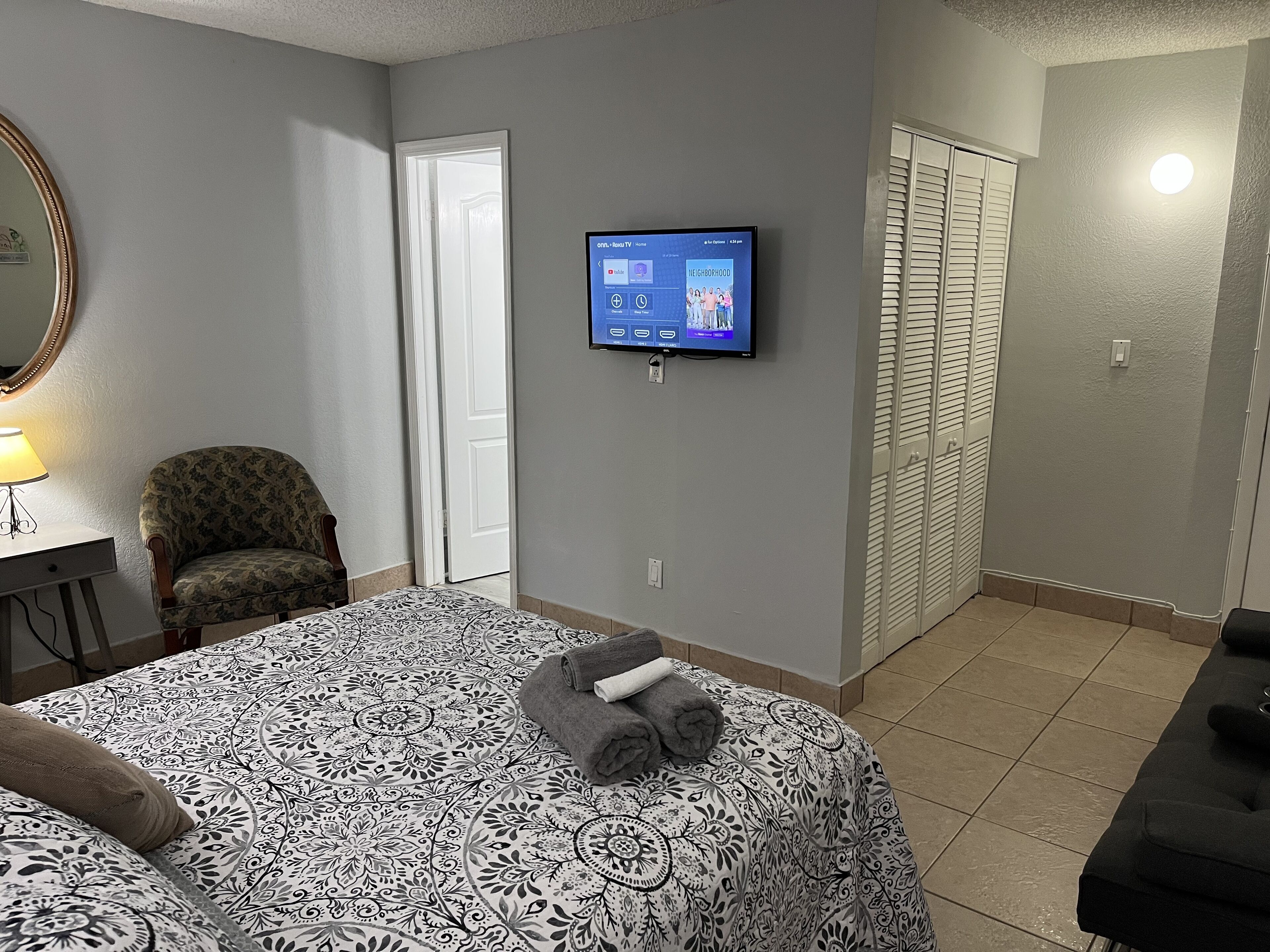A hotel room with a bed, a chair, a TV mounted on the wall, and a door leading to a closet.