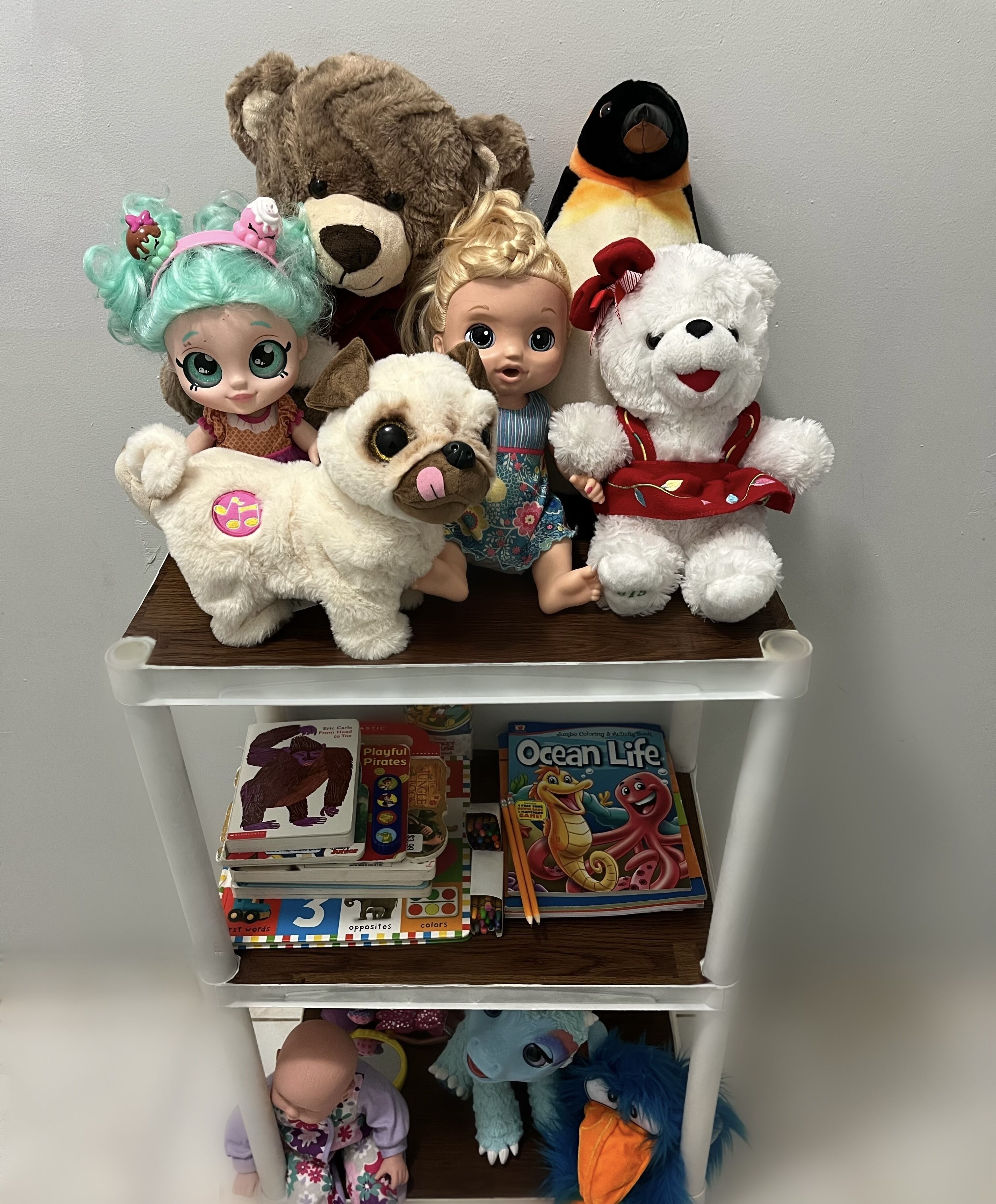 A shelf with various children's toys and books, including a white bear, a dog, and a penguin.