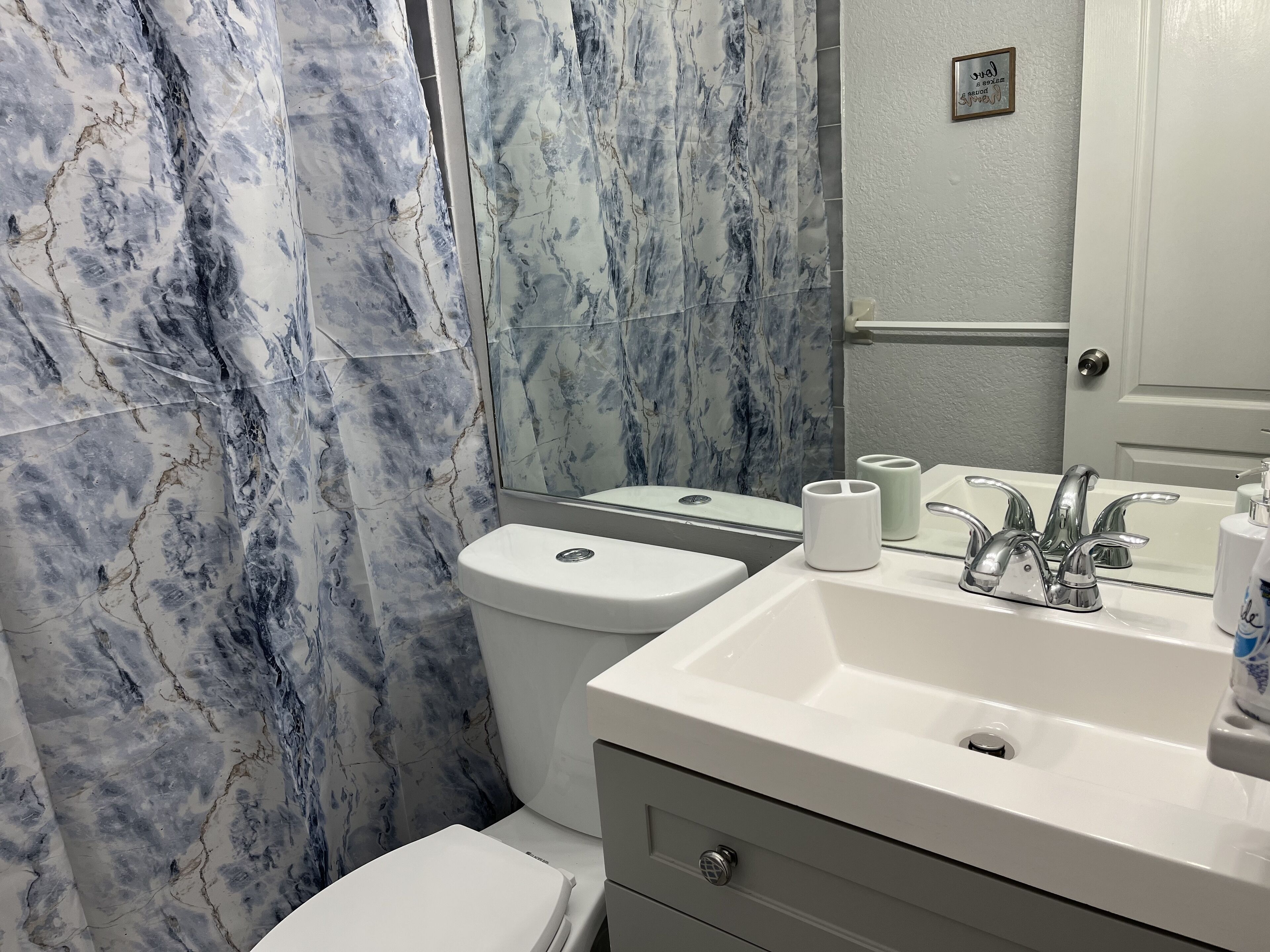 Un baño con pared de mármol, un inodoro, un lavabo con espejo y una puerta.