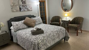 Ein Schlafzimmer mit einem Bett, zwei Stühlen, einem Nachttisch, einer Lampe und Wandbildern.