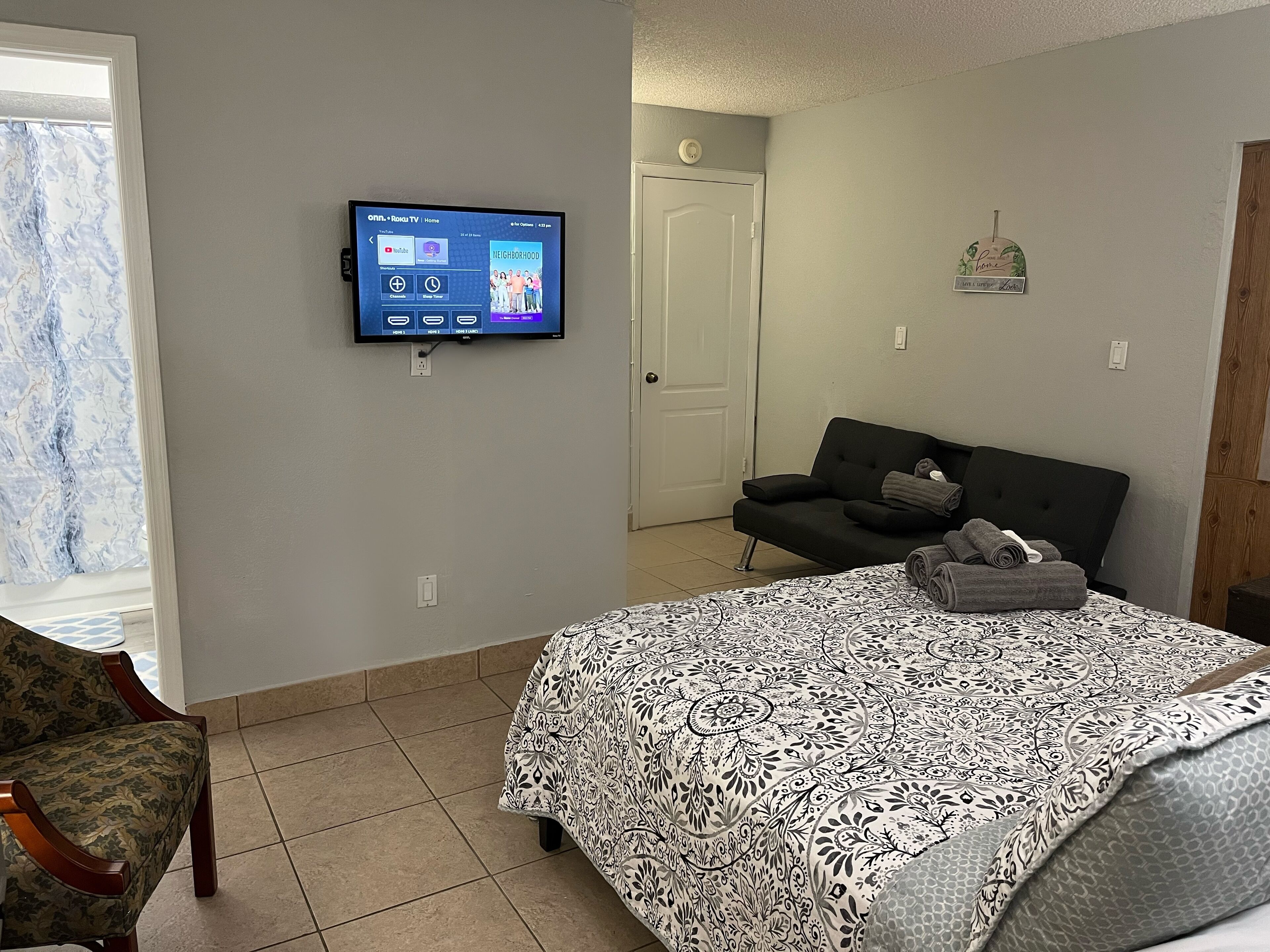 Ein Hotelzimmer mit Bett, einer Sitzecke, einem an der Wand befestigten Fernseher und einer Tür zu einem weiteren Raum.