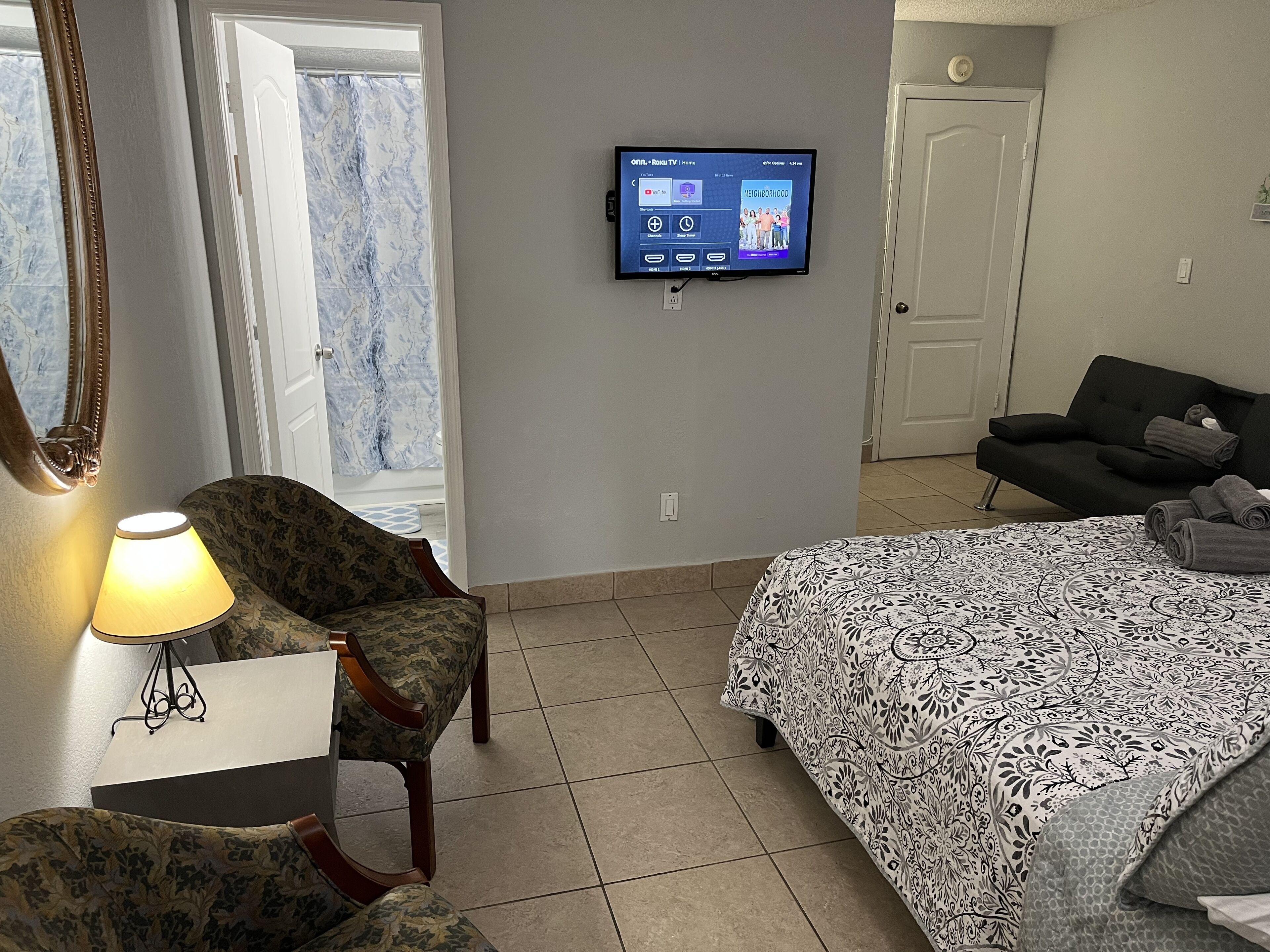 Une chambre d’hôtel avec un lit, une chaise, un téléviseur fixé au mur et une porte.