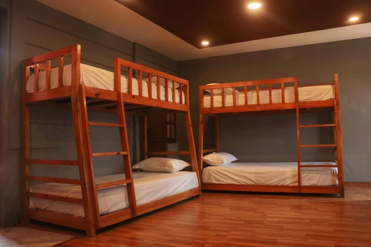 A room with three wooden bunk beds, a wooden floor, and a dark-colored wall.