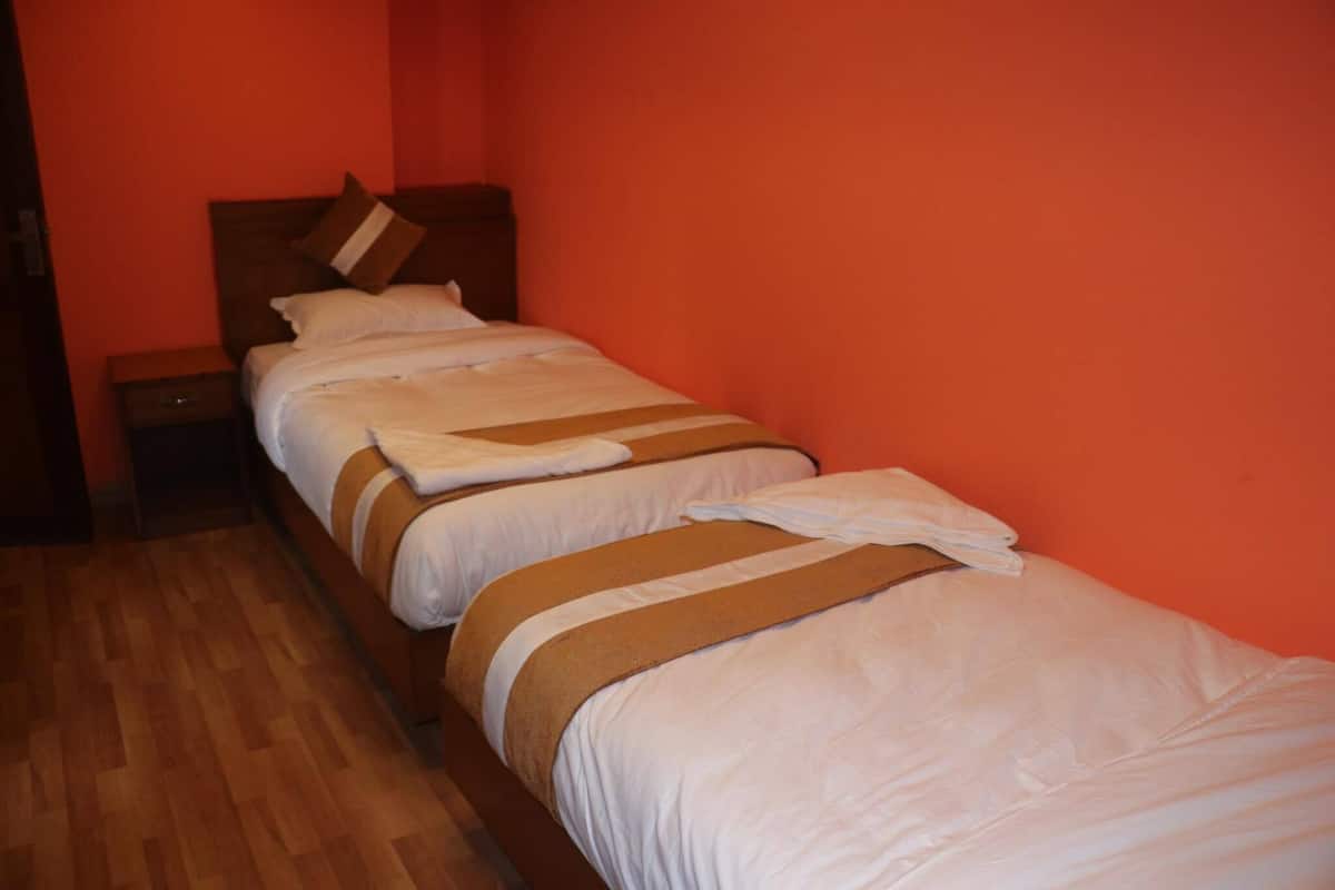 A single bed with a wooden headboard and white bedding in a room with orange walls and wooden flooring.