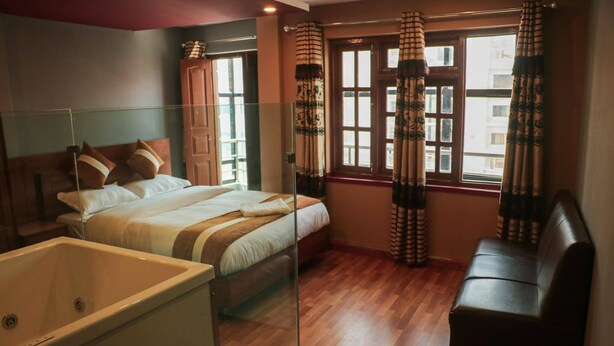 A bedroom with a bed, a sofa, a glass-enclosed bathtub, and a window with curtains. - Harrys Home  (Kathmandu)