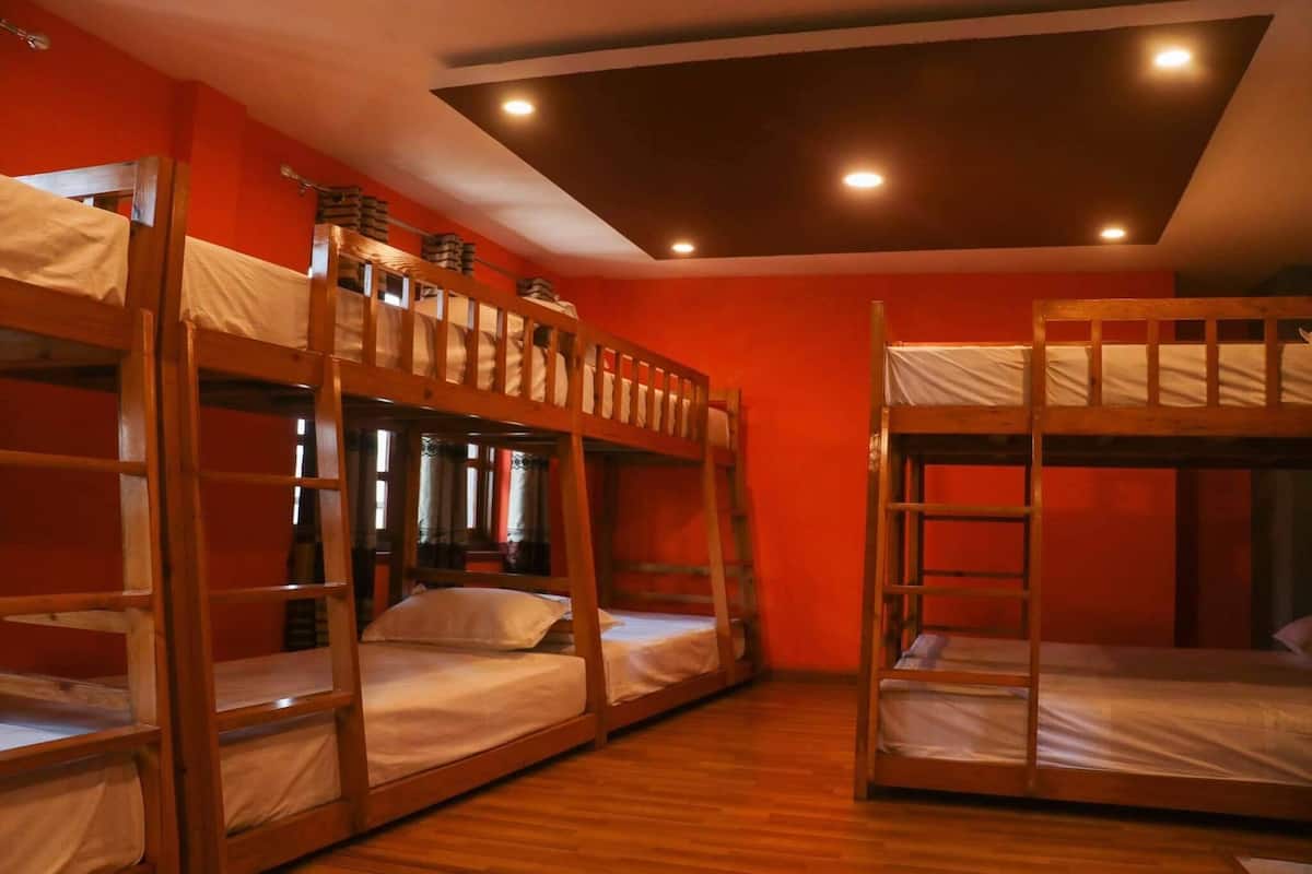 A room with bunk beds, wooden flooring, and a sloped ceiling with recessed lighting.
