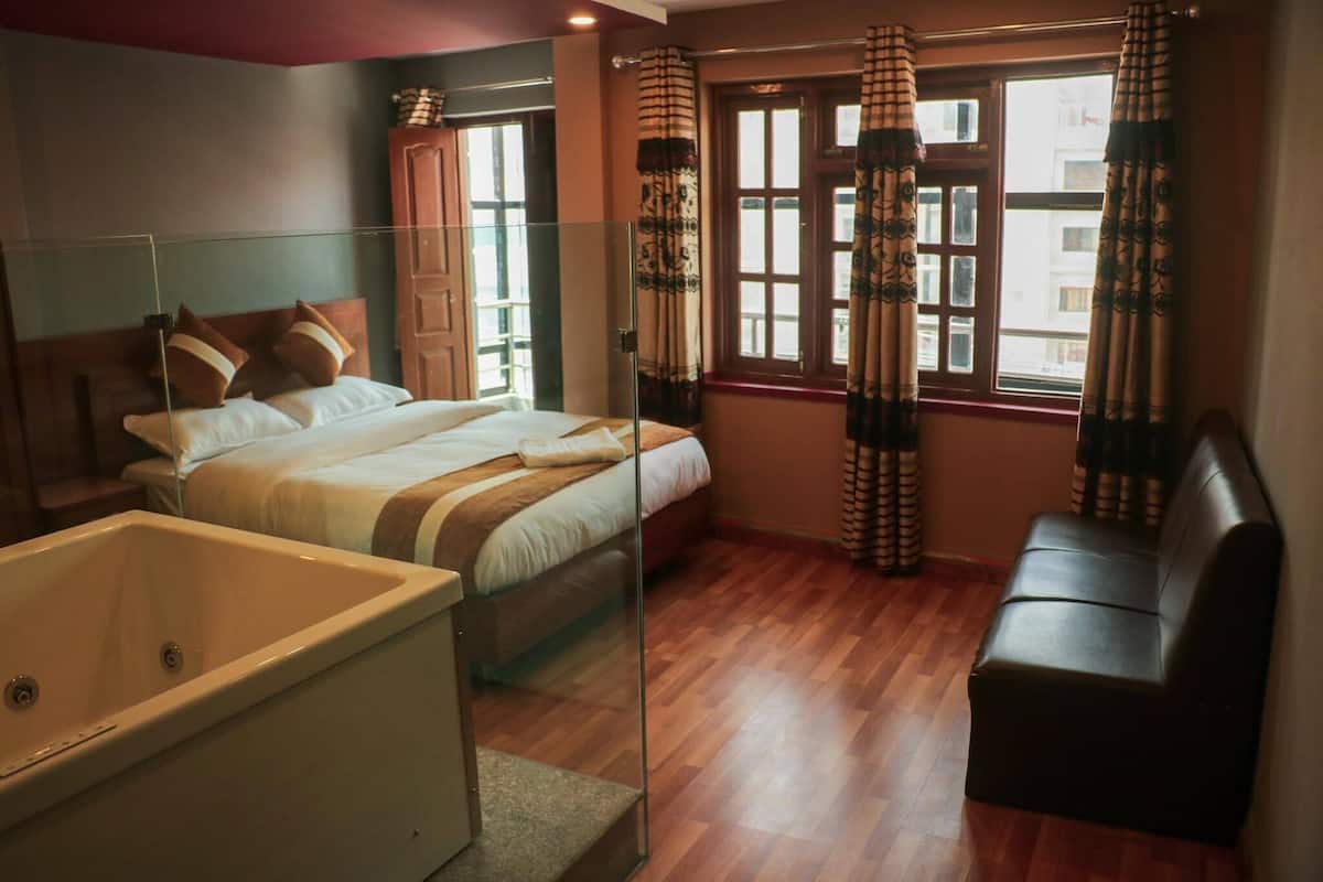 A bedroom with a bed, a sofa, a bathtub, and a window with curtains.