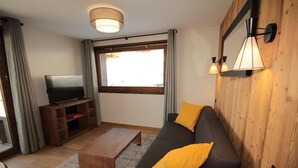 A living room with a sofa, a coffee table, a TV on a wooden stand, and a window with curtains. - 2nd floor, balcony, tv, 59m², Les Saisies (Hauteluce)
