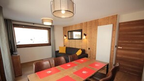 A modern room with a wooden dining table, red placemats, a sofa with yellow cushions, and a large window. - 2nd floor, balcony, tv, 59m², Les Saisies (Hauteluce)