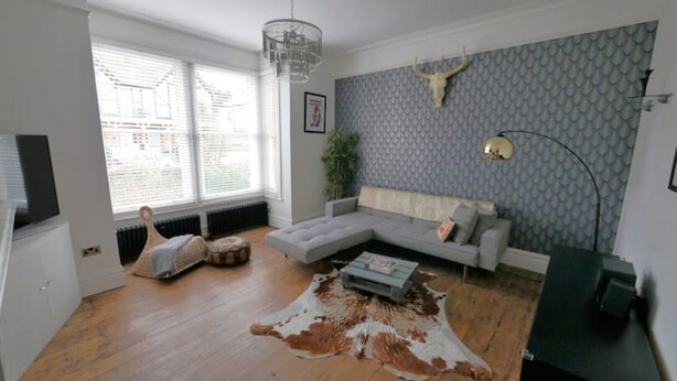A living room with a grey sofa, a cowhide rug, a hanging light fixture, and a wall-mounted deer head. - Trendy quirky ground floor Victorian garden flat (Worthing)