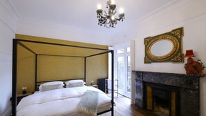 A four-poster bed in a room with a fireplace and a large mirror on the wall. - Trendy quirky ground floor Victorian garden flat (Worthing)