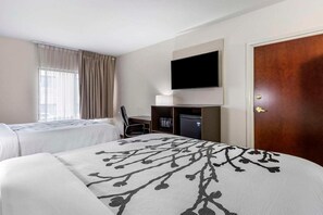 Une chambre d’hôtel avec deux lits, un téléviseur fixé au mur, un bureau avec une chaise et une porte.