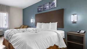 A hotel room with a large bed, a bedside table with a phone, a wall-mounted light, and a window with curtains. - Sleep Inn & Suites Grovetown - Augusta West (Grovetown)