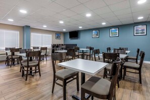 Uma área de jantar com mesas e cadeiras, uma televisão de tela plana na parede e quadros pendurados na parede.