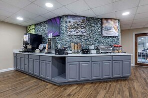 Un'area reception con un banco, macchine da caffè, un frigorifero e una parete decorativa con mosaici.