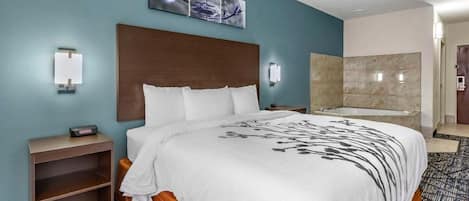 Une chambre d’hôtel dotée d’un grand lit, d’une tête de lit, d’une œuvre d’art accrochée au mur, d’une table de chevet et d’une salle de bain avec baignoire, le tout sur un plancher recouvert de moquette.