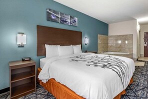 Habitación de hotel con una cama grande, cabecero, una obra de arte en la pared, mesita de noche, baño con bañera y piso alfombrado.
