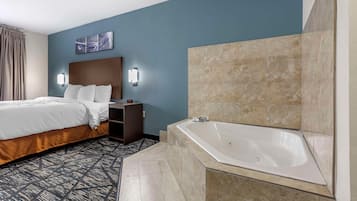 A hotel room with a bed, a nightstand, a wall-mounted light, a painting, and a bathroom with a bathtub.