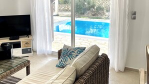 A room with a sofa, TV, and a view of a swimming pool. - Modern villa with private pool - 120 m from Verde Blue beach (Μπαρμπάτι)