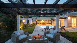 An outdoor patio area with wicker furniture, a glass table, and a pool in the background. - Modern villa with private pool - 120 m from Verde Blue beach (Μπαρμπάτι)