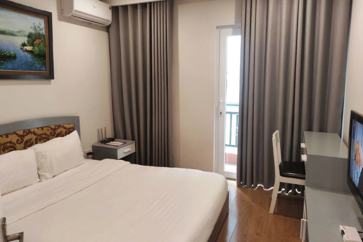 Une chambre d’hôtel avec un grand lit, un bureau avec une chaise, un appareil de climatisation, un tableau au mur et un téléviseur.