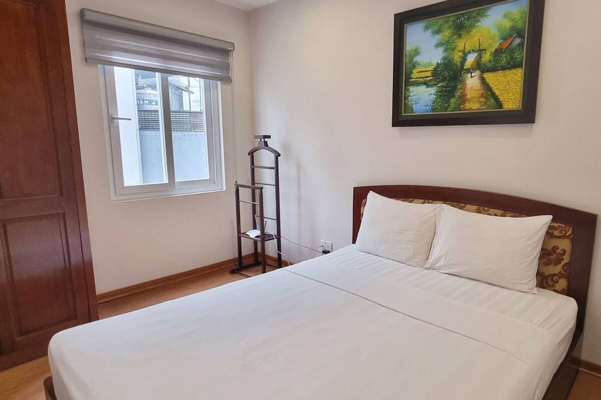 Une chambre à coucher avec un lit, une fenêtre avec des stores, un tableau au mur et une armoire en bois.