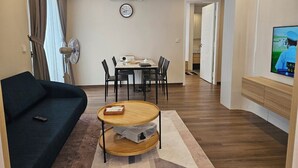 A living room with a sofa, a small wooden table, a dining table with chairs, a TV, and an air conditioning unit.