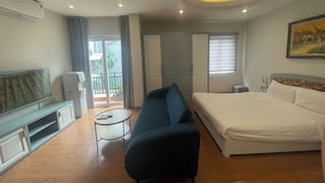 A hotel room with a bed, a sofa, a TV, a small table, and a balcony.