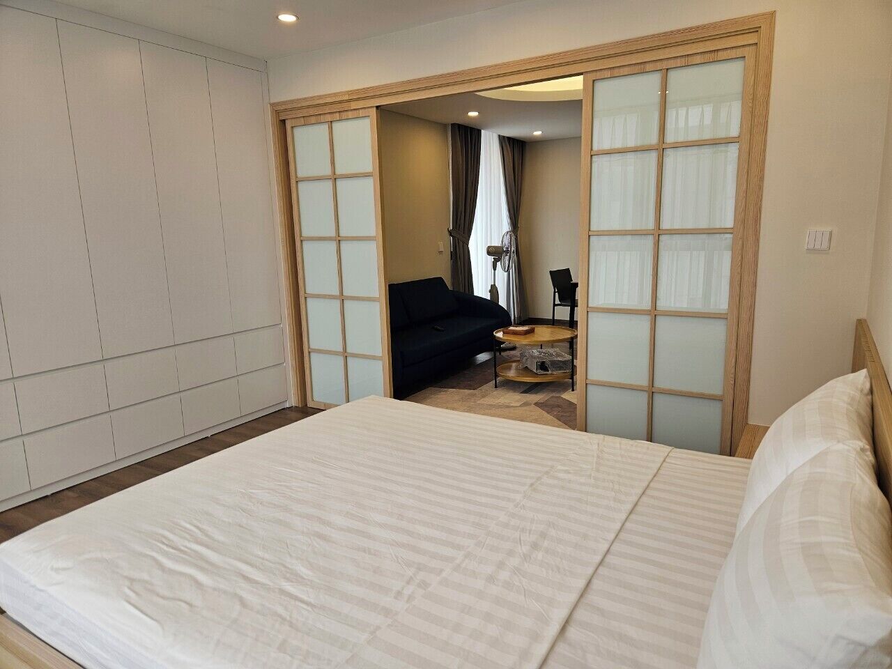 A hotel room with a large bed, a small round table, and a sofa in the background.