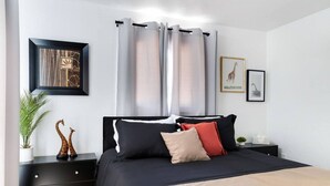 A modern bedroom with a black bed, beige and red pillows, a black nightstand, a framed picture of a giraffe, and a potted plant. - Weber · Jungle House, minutes away from ASU/ Old Town (Tempe)